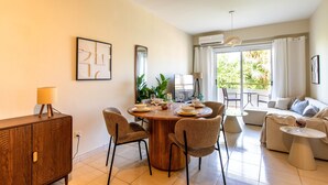 A modern living room with a dining area, a sofa set, and a view of greenery outside. - Veta 31 . 1-BR Apt. & Balcony in Larnaca (Larnaca)