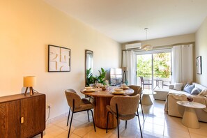 A modern living room with a dining area, a sofa set, and a view of greenery outside. - Veta 31 . 1-BR Apt. & Balcony in Larnaca (Larnaca)
