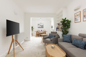 A modern living room with a flat-screen TV, a sofa, a coffee table, and a dining area with a table and chairs. - New! Bright 2BR Duplex w/Patio in Pimlico (Greater London)