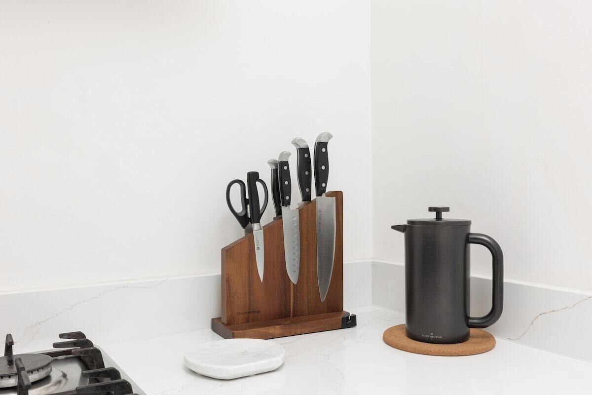 A kitchen counter with a knife block, a coffee press, and a white scale.