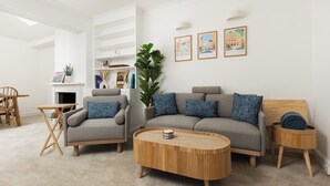 A modern living room with a sofa, armchairs, a coffee table, and a side table. There is a fireplace, a plant, and framed pictures on the wall. - New! Bright 2BR Duplex w/Patio in Pimlico (Greater London)