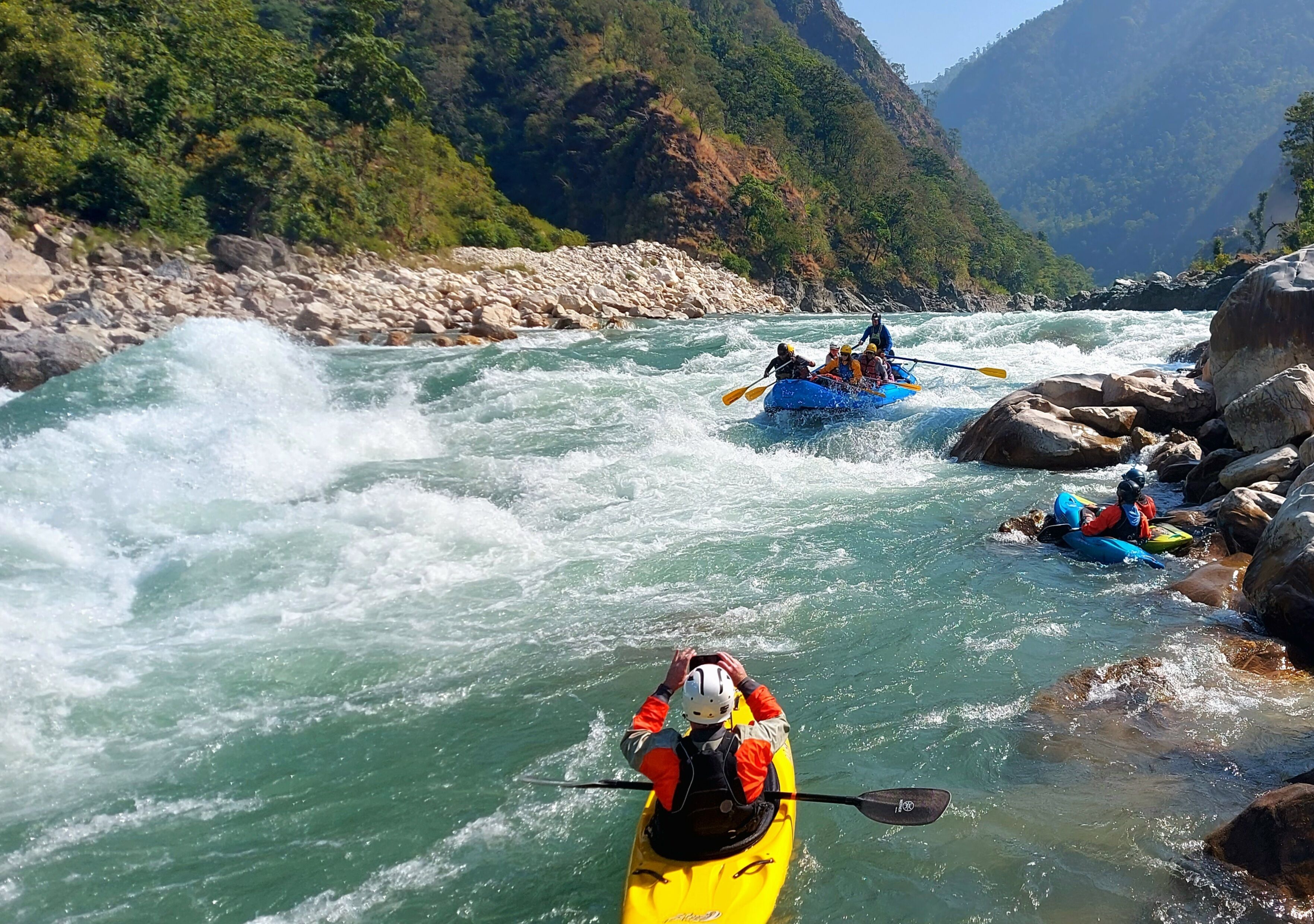 Eine Gruppe Kajakfahrer auf einem Fluss mit steinernen Ufern und üppigem Grün im Hintergrund.