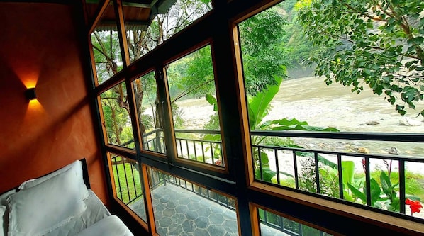 Una habitación con cama, ventana y vista al río y follaje.