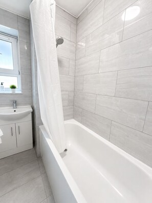 A modern bathroom with a bathtub, a sink, and a shower. - Compact Double Room near Tower Bridge & Metro (London)