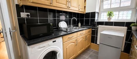 Una cocina compacta con lavadora, microondas, refrigerador y armarios de madera.