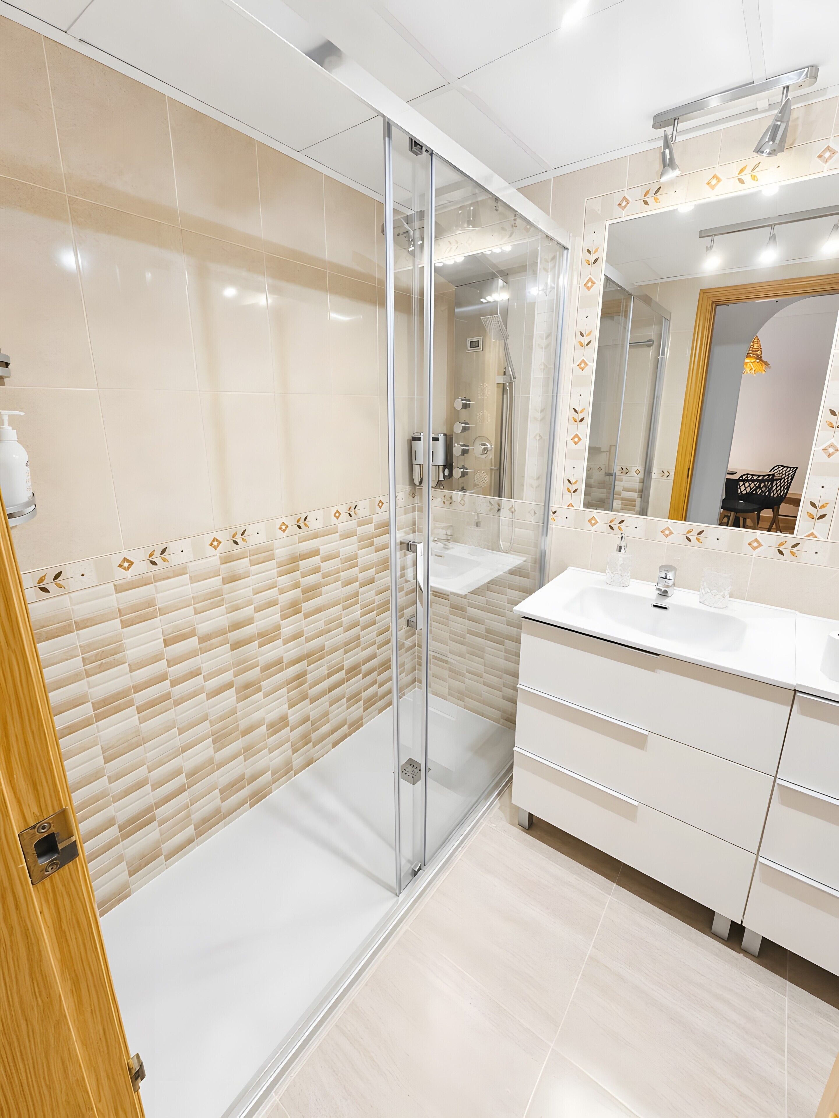 A modern bathroom with a glass-enclosed shower, a white sink, and a large mirror with a decorative frame.