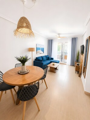 A modern living room with a round wooden dining table, blue sofa, and a hanging woven light fixture. - Apartment 'Arena & Mar' with Private Pool, Wi-Fi and Air Conditioning (Cartagena)