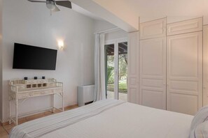 A bedroom with a bed, a TV mounted on the wall, a white bedside table, and a sliding glass door leading to an outdoor area. - Aelia Villa Aegina, Villa (Aegina)