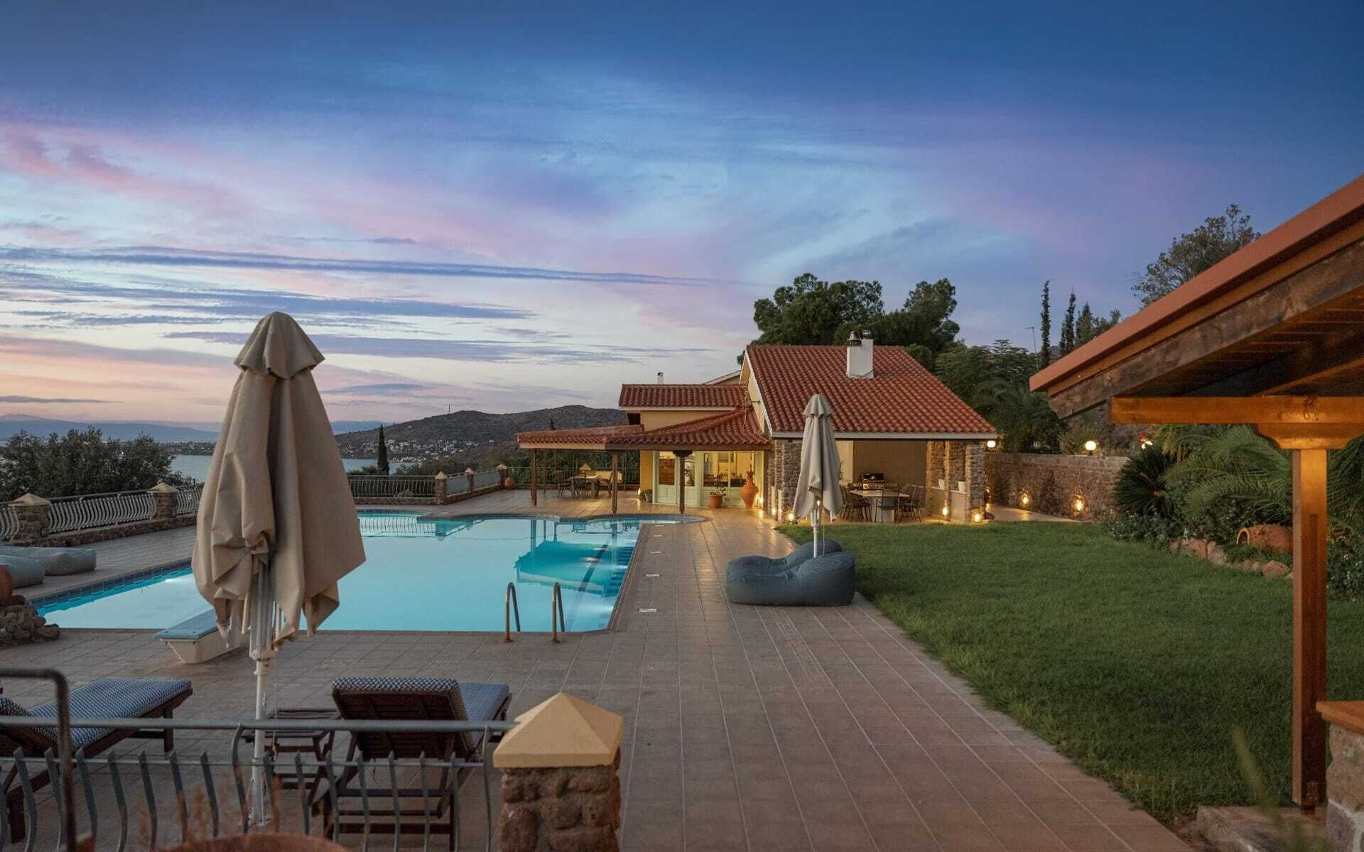 Une piscine avec des chaises longues et des parasols, un patio couvert et une vue sur un paysage vallonné.
