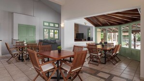 A dining area with wooden tables and chairs, a television, and a stone wall. - Aelia Villa Aegina, Villa (Aegina)