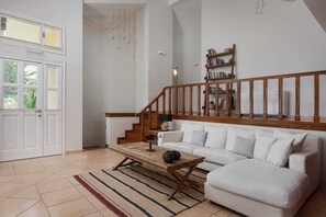 Ein Wohnzimmer mit einem weißen Sofa, einem Holztisch, einem Streifen Teppich, einer Holztreppe mit Geländer und einem Bücherregal.