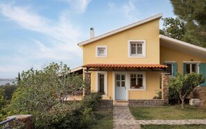 A two-story house with a yellow facade, a tiled roof, and a stone pathway leading to the entrance. - Aelia Villa Aegina, Villa (Aegina)