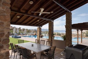 An outdoor patio with a pool, stone pillars, a table with chairs, and a grill. - Aelia Villa Aegina, Villa (Aegina)