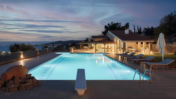 A swimming pool with a view of the sea, a patio area with lounge chairs, and a stone wall. - Aelia Villa Aegina, Villa (Aegina)