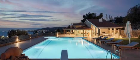 Una piscina con vistas al mar, un área de patio con sillones de descanso y un muro de piedra.