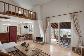 A spacious living area with a fireplace, a dining table, and a balcony with outdoor seating. - Aelia Villa Aegina, Villa (Aegina)