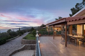 Une terrasse avec des meubles d’extérieur, un chemin en pierre et une vue sur la mer et les collines.