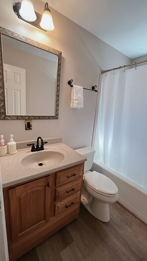 A bathroom with a wooden vanity, a white toilet, a shower curtain, and a mirror with wall sconces. - Cozy Tahoe Retreat 3BR 2BA Minutes to Lake Tahoe (South Lake Tahoe)