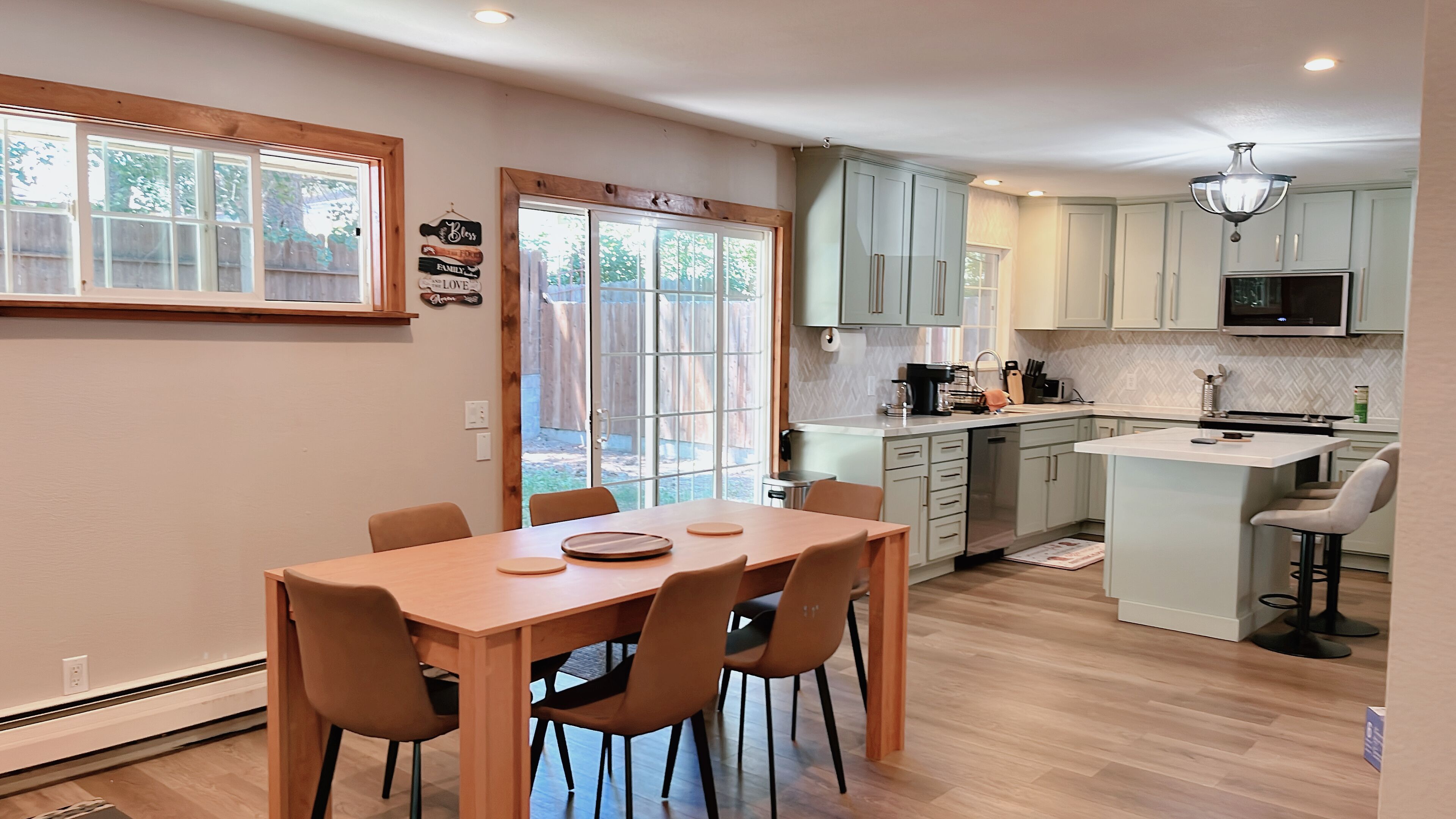 A modern kitchen with a dining area, wooden flooring, and light-colored cabinetry.