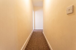 A narrow hallway with carpeted flooring and a light switch on the wall. - 3-Bed Townhouse Sleeps 5 · Walk to Designer Outlet & STEAM Museum (Swindon)
