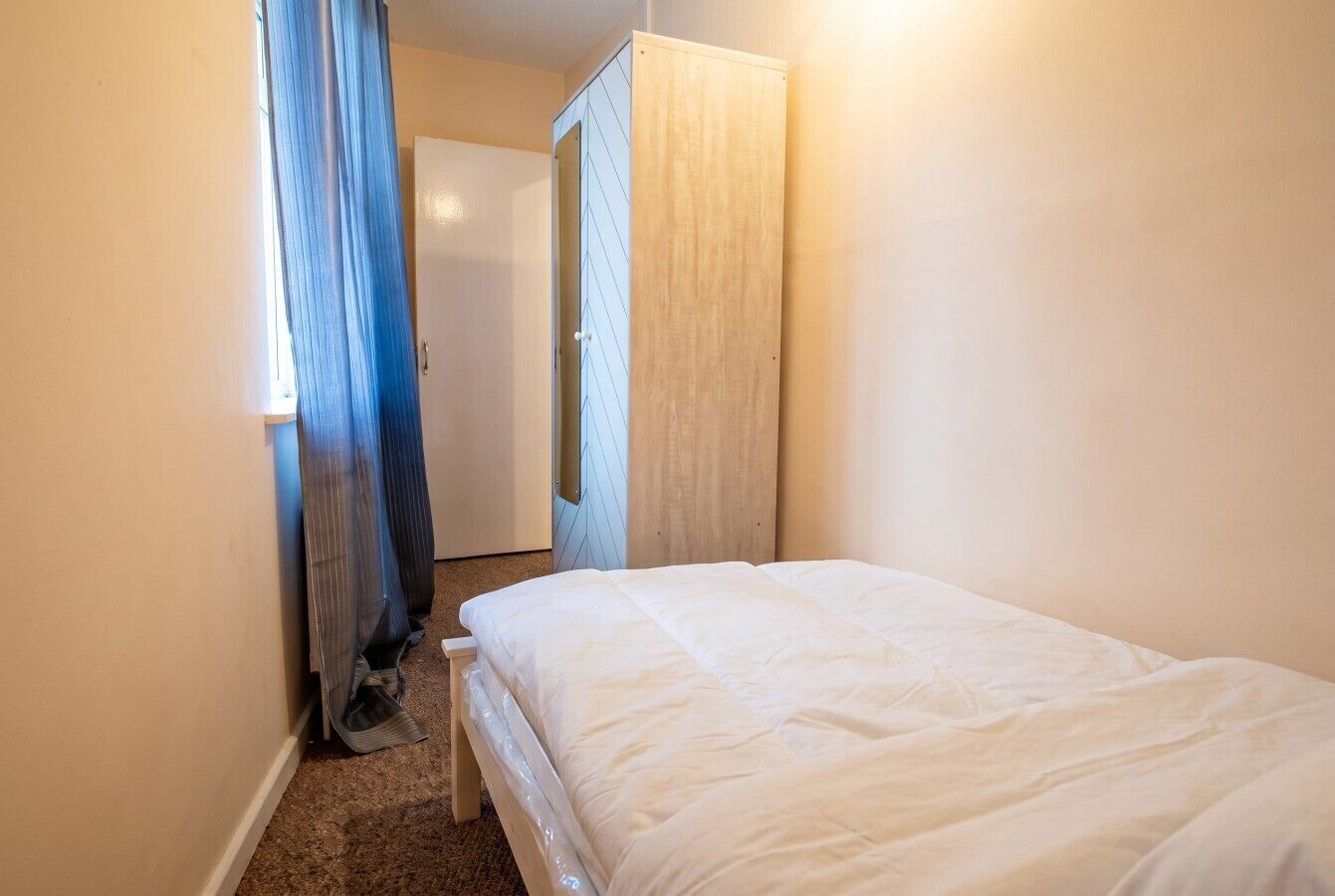 Ein Schlafzimmer mit einem Bett, einem Kleiderschrank und einer Tür zu einem weiteren Raum.
