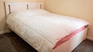 Ein Einzelbett mit weißem Kopfteil und rosa Matratze.