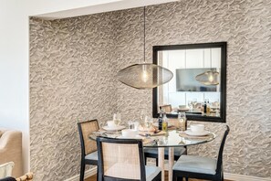 A dining area with a round table, four chairs, and two pendant lights. - Camps Bay 2 Bed with Sea Views Shoreline Views (Cape Town)