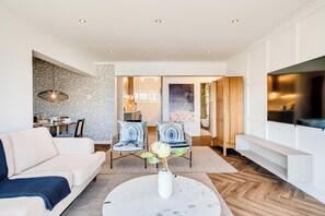 A modern living room with a sofa, chairs, a coffee table, and a dining area. - Camps Bay 2 Bed with Sea Views Shoreline Views (Cape Town)