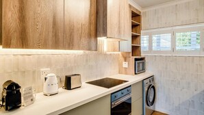 Une cuisine moderne avec des meubles en bois, un four à micro-ondes encastré, une machine à café, un grille-pain et un lave-linge.