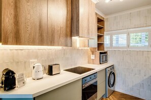 Eine moderne Küche mit Holzausstattung, einer eingebauten Mikrowelle, einer Kaffeemaschine, einem Toaster und einer Waschmaschine.