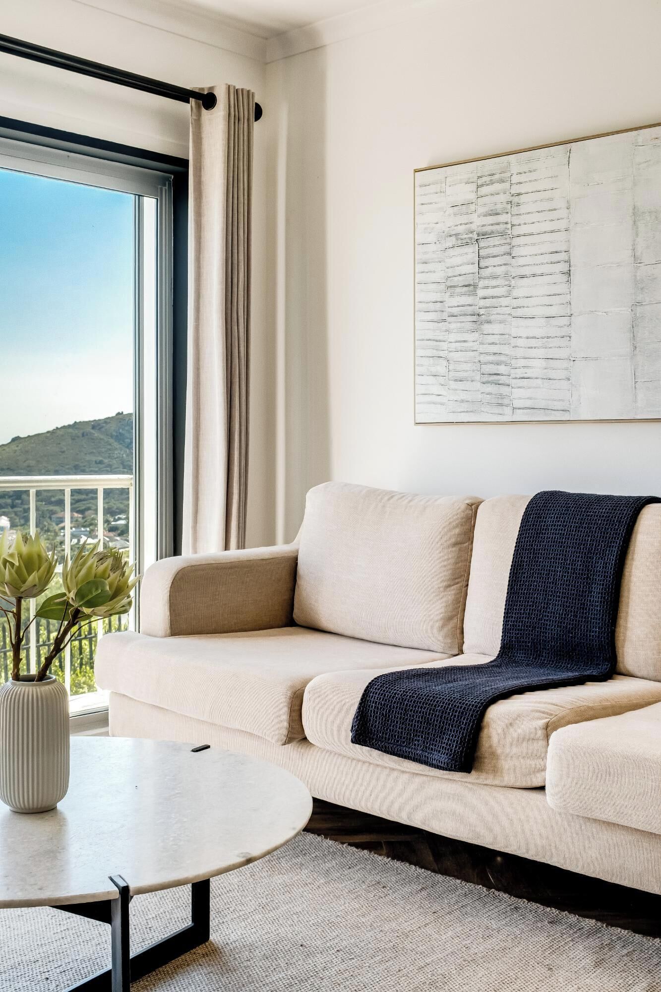A modern living room with a beige sofa, a round coffee table, and a view of a mountain through a large window.