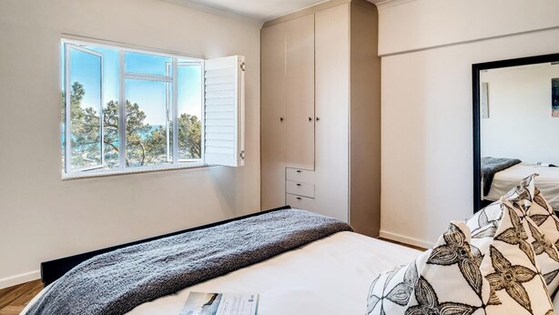 Une chambre avec une grande fenêtre, un lit recouvert d’une couvre-lit à motifs et une armoire.