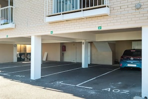 A parking garage with multiple levels, marked parking spaces, and a blue car parked on the upper level. - Camps Bay 2 Bed with Sea Views Shoreline Views (Cape Town)