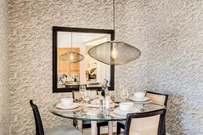 A dining area with a round glass table, two wicker chairs, and a large mirror above the table. - Camps Bay 2 Bed with Sea Views Shoreline Views (Cape Town)