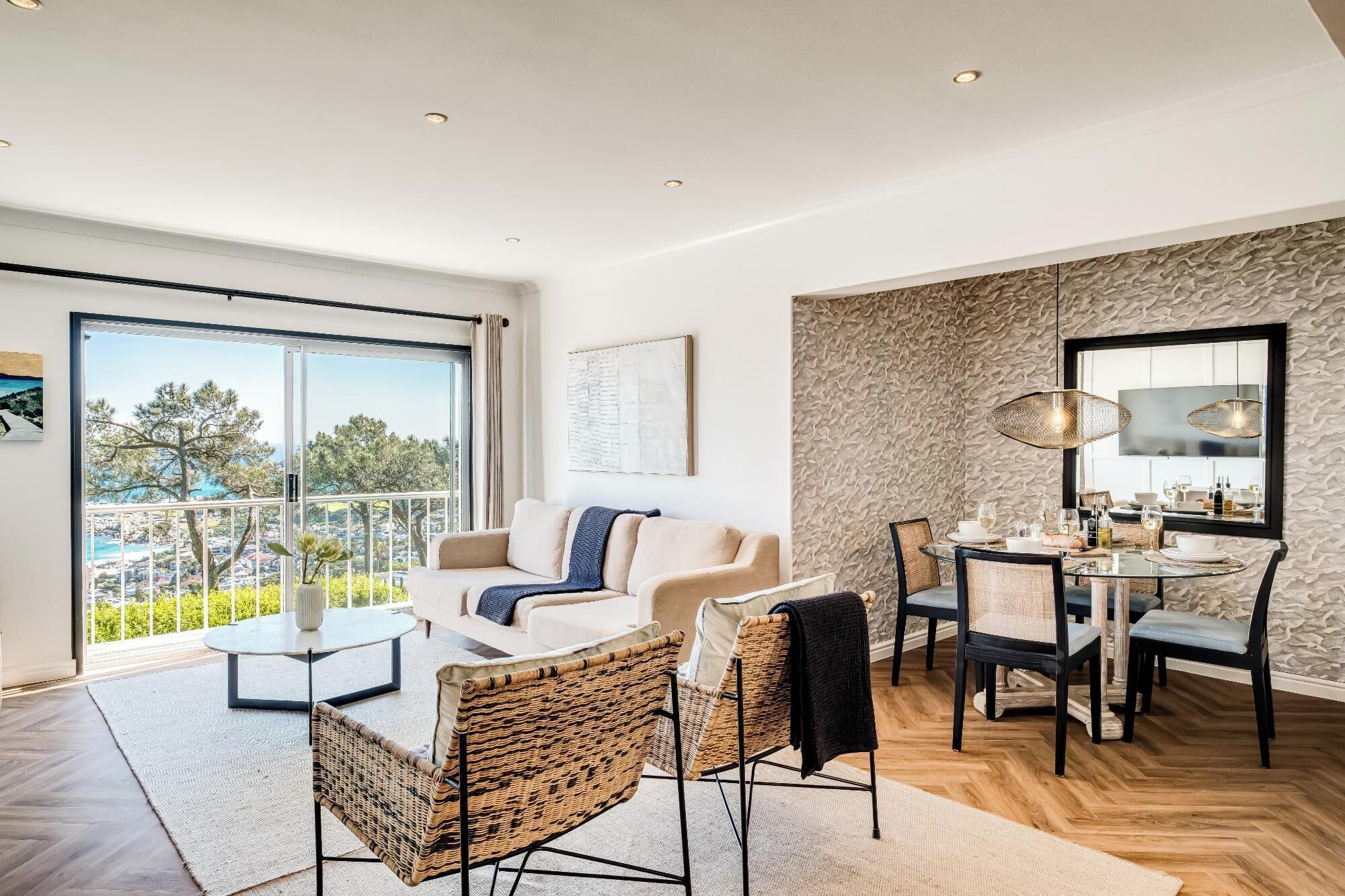Ein modernes Wohnzimmer mit Sofa, Sesseln, Esstisch und einem Balkon mit Blick.