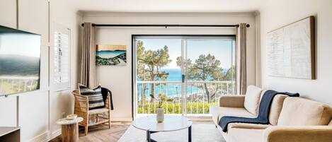 Ein geräumiges Wohnzimmer mit großem Fenster, einer Couch, einem Couchtisch und einem Fernseher.