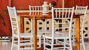 A dining area with a wooden table and white chairs, a lantern, and two hats on the wall. - Baobab Garden Studio with pool Watamu (Watamu)