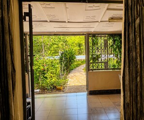 Ein offenes Durchgang zu einer gefliesten Terrasse mit Blick auf einen Garten und ein Schwimmbad.