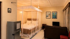 A hotel room with a four-poster bed, a television, a sofa, and a small table. - Baobab Garden Studio with pool Watamu (Watamu)