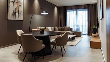 A modern living room with a round dining table, beige sofas, and a large window with curtains.