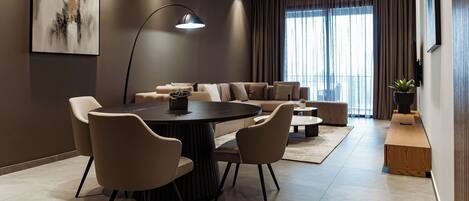 Una sala de estar moderna con una mesa de comedor redonda, sofás color beige y un ventanal con cortinas.