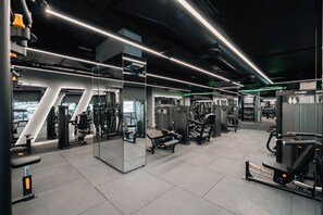 A modern gym with various exercise equipment, mirrored walls, and bright overhead lighting. - ICON RESIDENCES Douala (Douala)