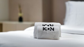 Una cama bien hecha con una almohada blanca y una toalla doblada con el texto 'ICON ICON'.