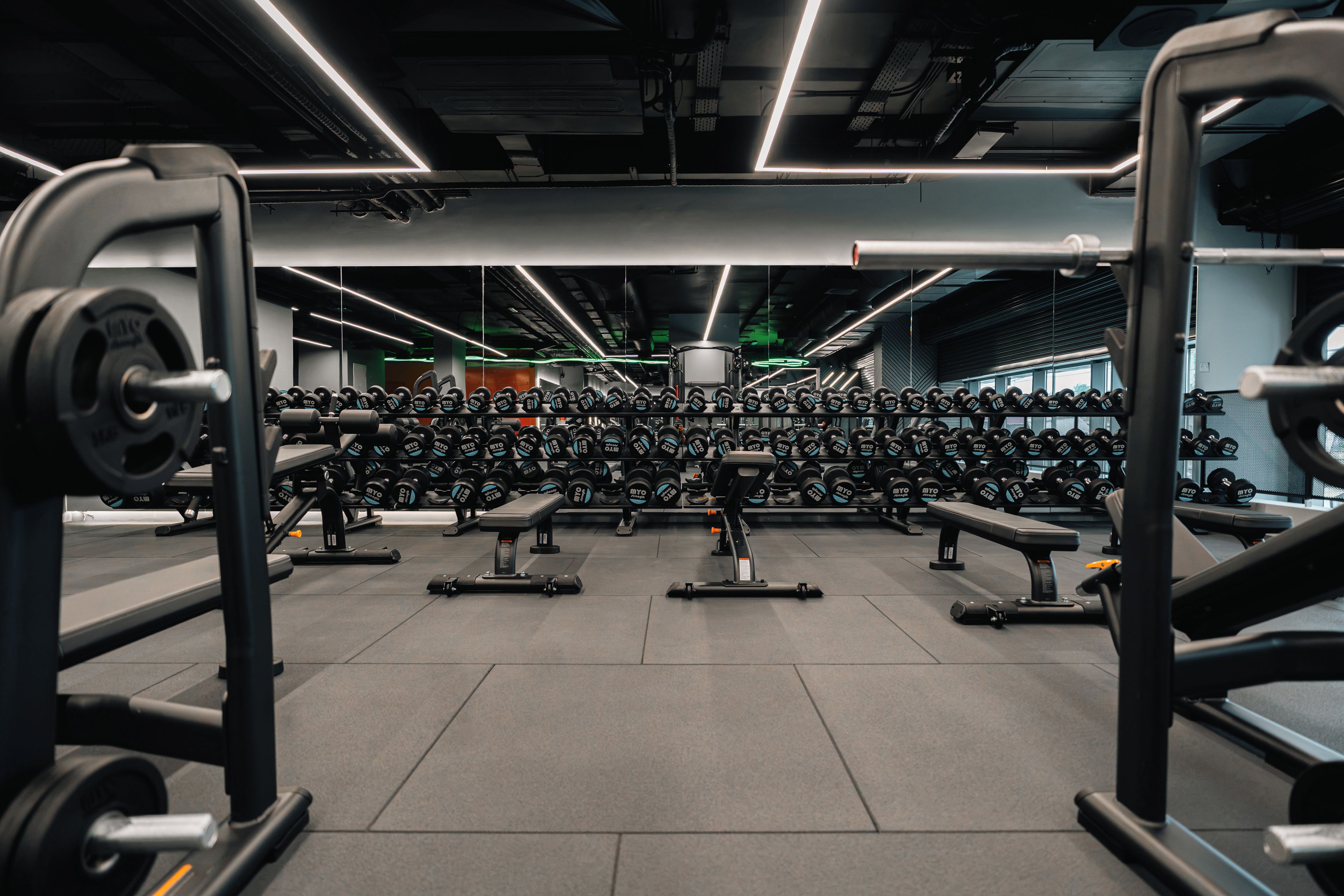Un gimnasio con varias estaciones de levantamiento de pesas, bancos y una variedad de mancuernas.