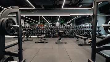 Un gimnasio con varias estaciones de levantamiento de pesas, bancos y una variedad de mancuernas.