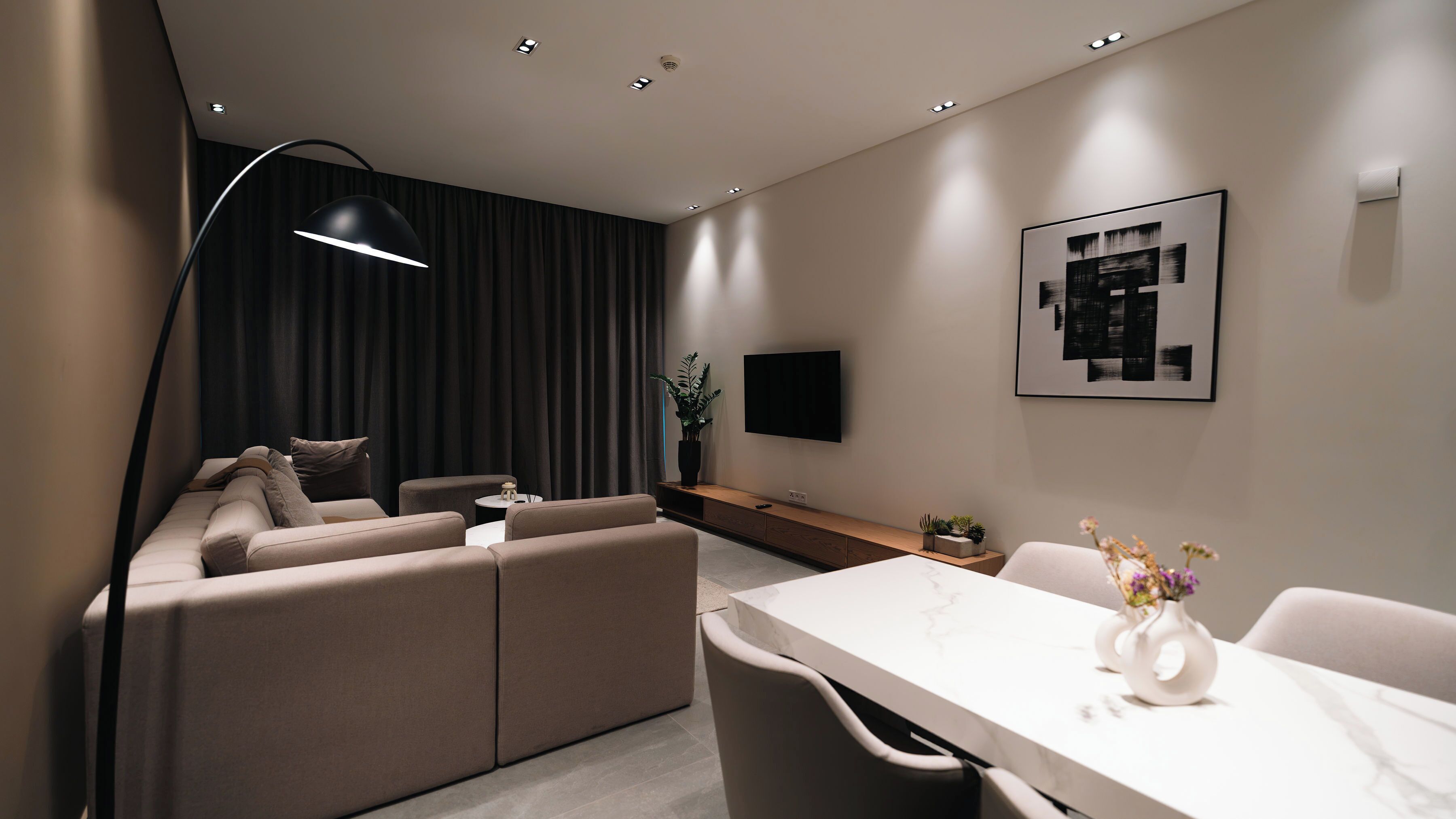 Una sala de estar moderna con un sofá, una mesa de comedor, un televisor montado en la pared y una lámpara de pie.