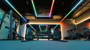 A gym with exercise equipment, weight racks, and neon lighting.