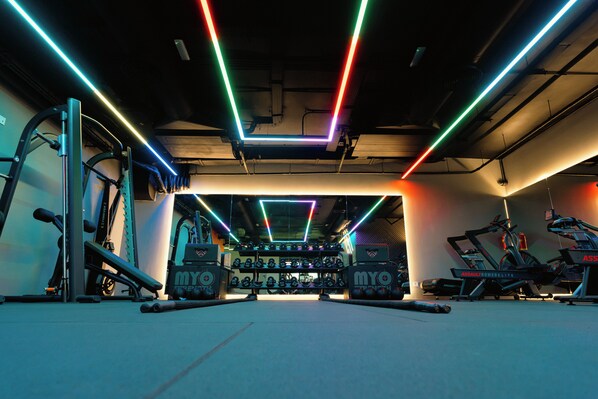 Une salle de sport équipée de machines d’exercice, de supports pour les poids et dotée d’un éclairage néon.