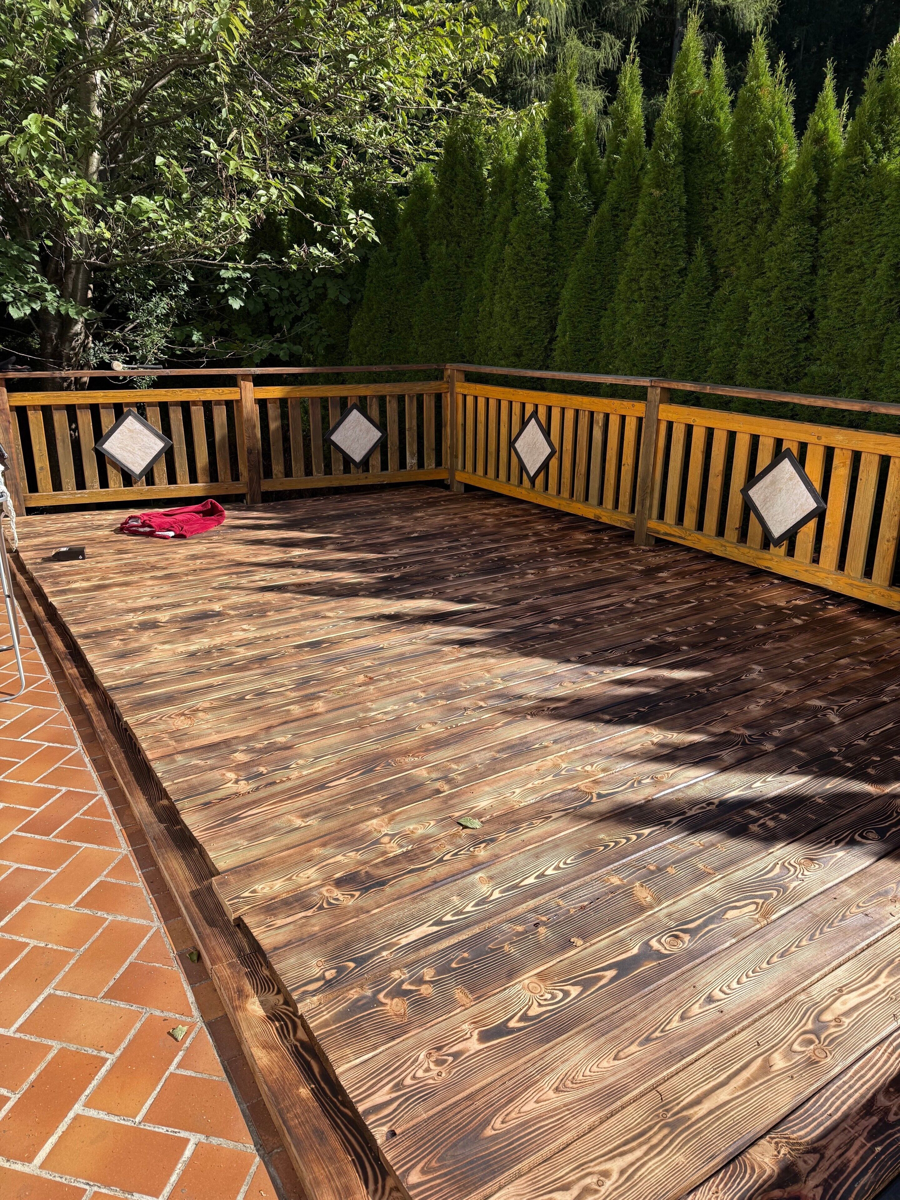A wooden deck with a brick border, surrounded by a wooden fence with diamond-shaped cutouts.