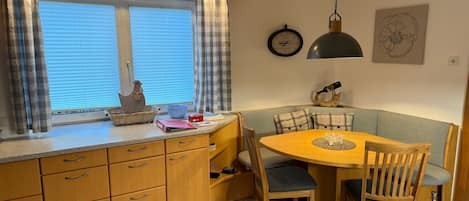 A compact kitchen with a dining area, featuring a wooden cabinet, a round table, and a bench.